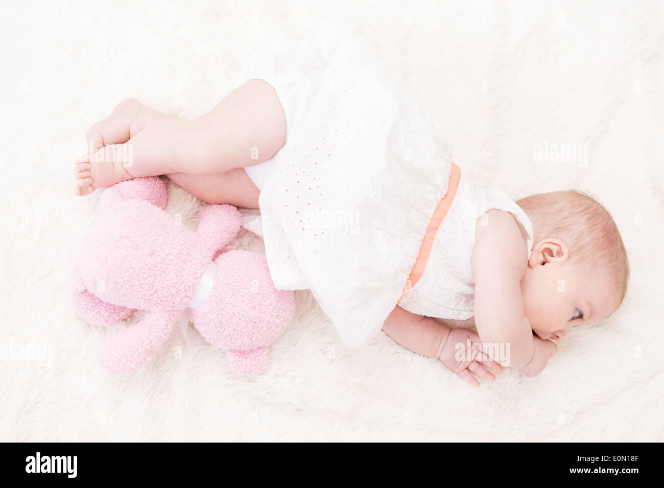 Baby girl in white dress playing on white blanket. Stock Photo