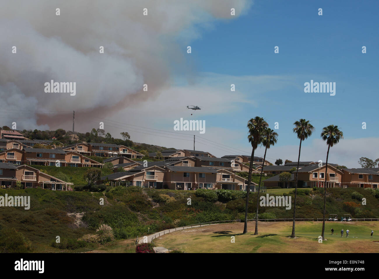 San Clemente, California, USA. 16th May, 2014. San Clemente residents play golf as fire fighting aircraft douse the nearby Las Pulgas wildfire inside Camp Pendleton marine Base. The wildfire in the western region of Camp Pendleton has grown to 8,000 acres burned, base officials confirmed, known as the Las Pulgas Fire, is 5 percent contained, officials said. California firefighters have continued to battle wildfires, which have scorched more than 11,000 acres and caused thousands to evacuate. Credit:  ZUMA Press, Inc./Alamy Live News Stock Photo