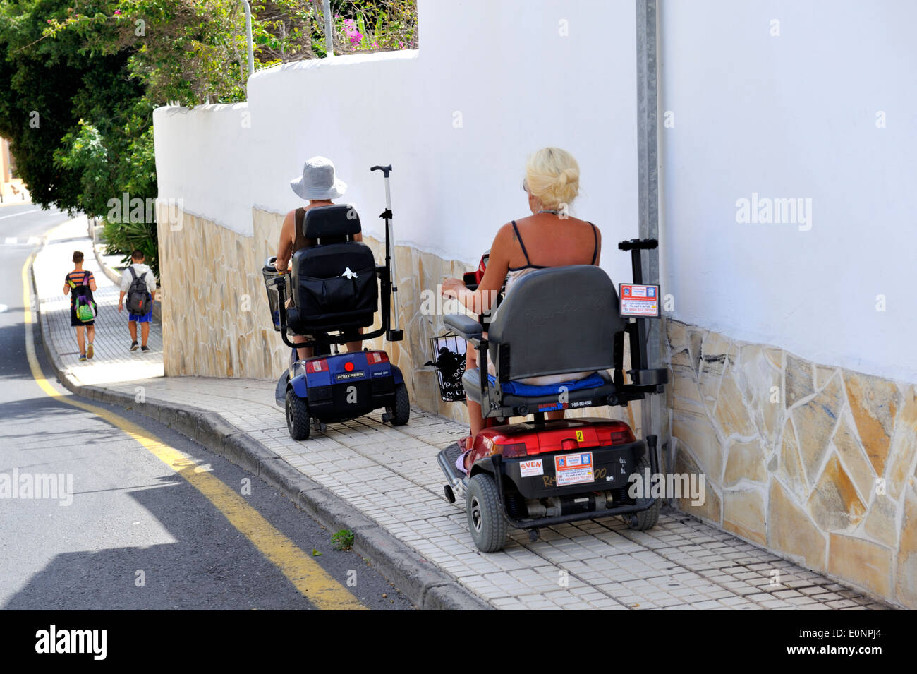 Two women on hired electric mobility scooters on pavement of Los Cristinos, Tenerife Stock Photo