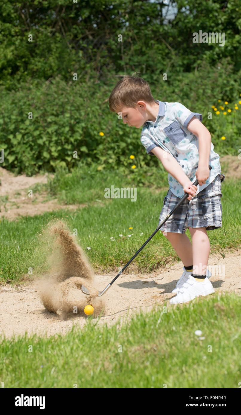 Little boy aged 5 years and a keen golfer playing out of a bunker using a specially cut down sized golf club. Hampshire England Stock Photo