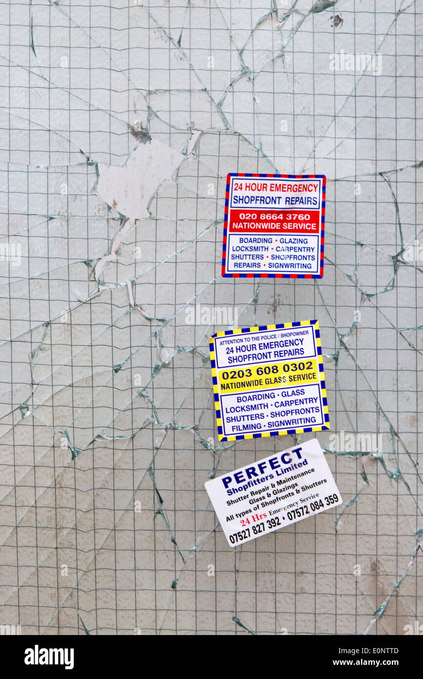 Broken shop door window with advertising stickers from several 24 Hour Emergency Shopfront Repair companies, Waterloo, London UK Stock Photo