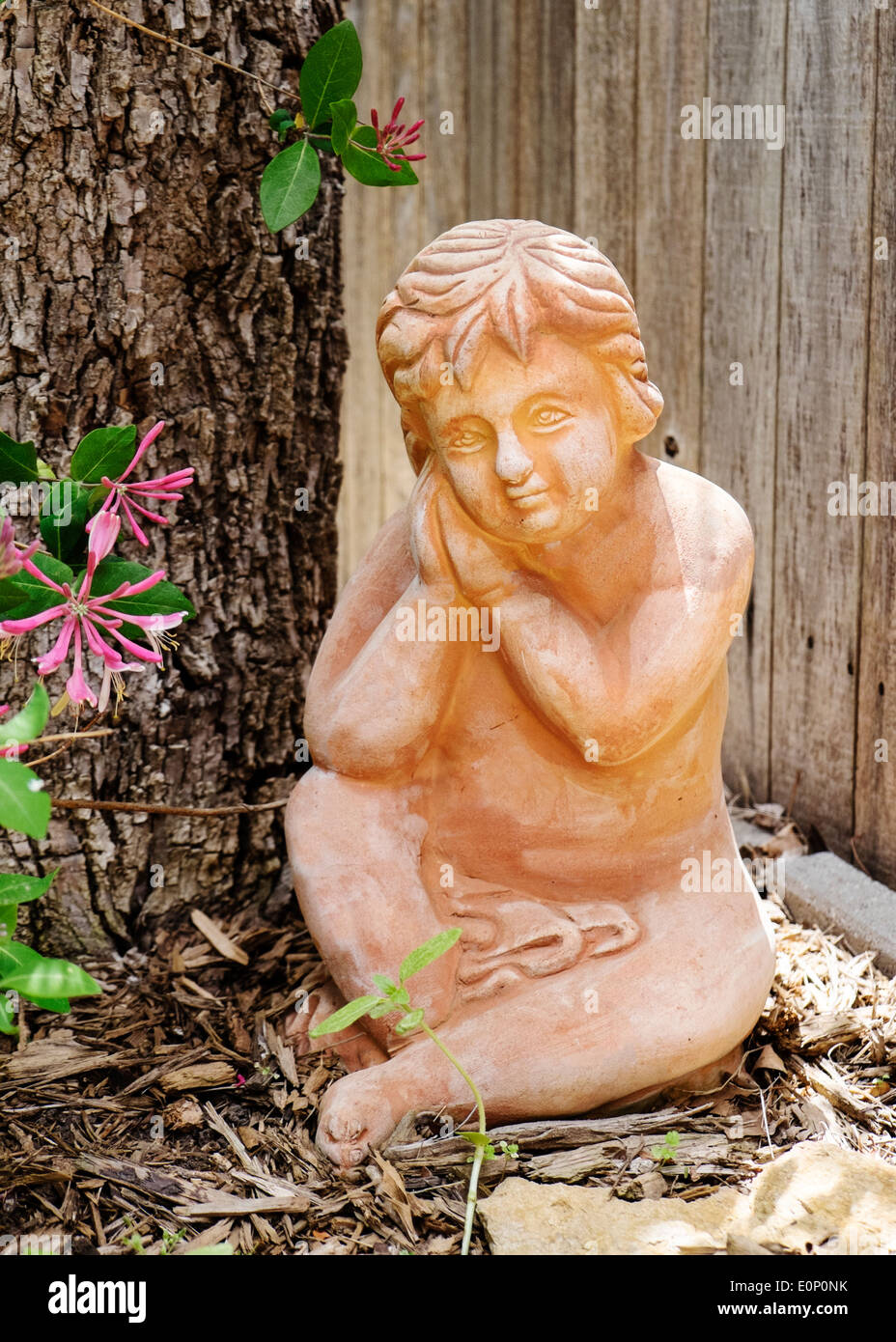 Ornamental garden statuary of a cherub next to a tree in a home's back yard. Stock Photo