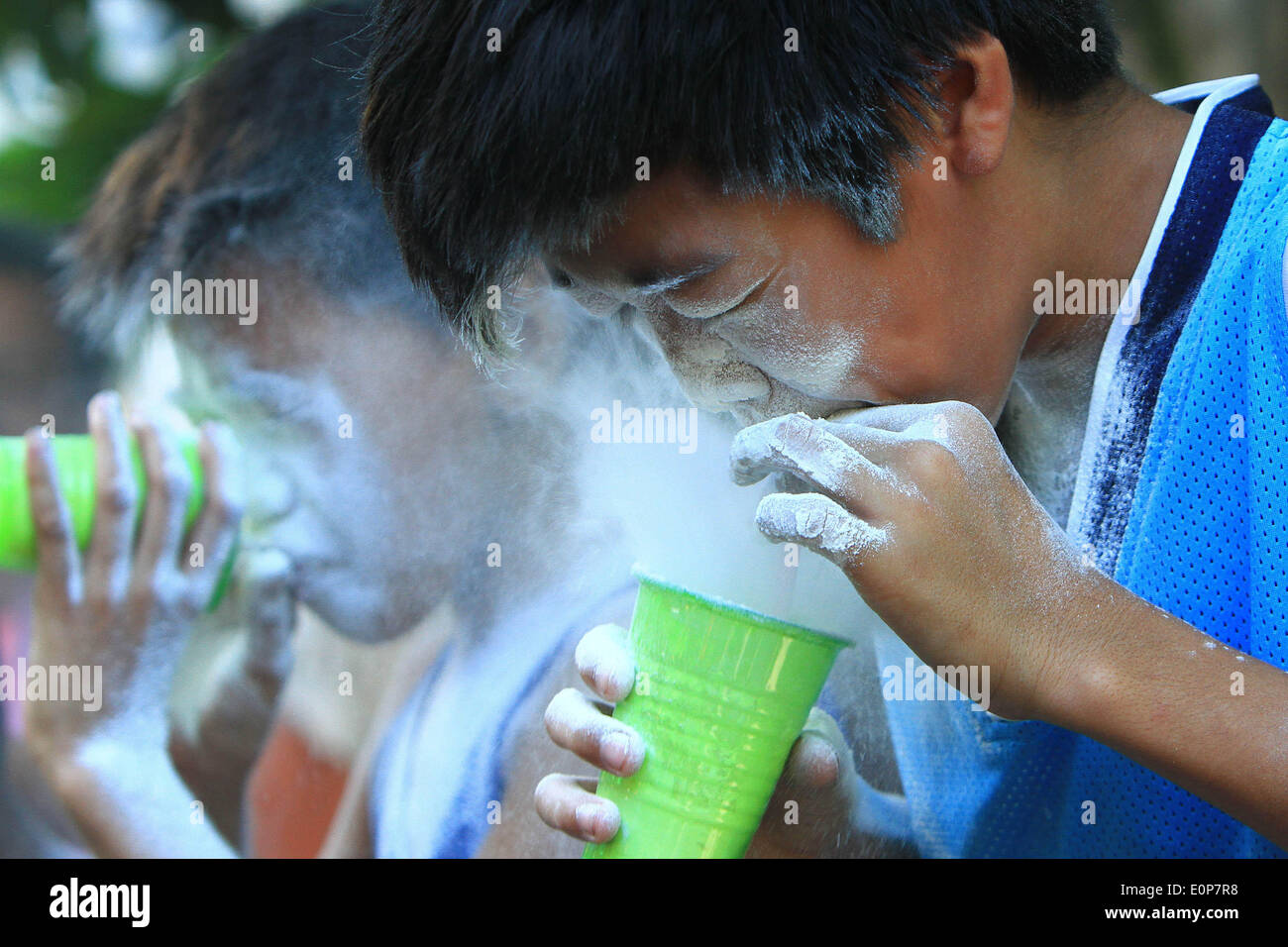 Paranaque City, Philippines. 18th May, 2014. Children try to empty their cups by blowing the flours out as they participate in a parlor game during the feast day of Saint Rita de Cascia in Paranaque City, the Philippines, May 18, 2014. The Saint Rita de Cascia Festival is commemorated through parades, games and splashing of water to each other to give thanks for the good fortune. Credit:  Rouelle Umali/Xinhua/Alamy Live News Stock Photo