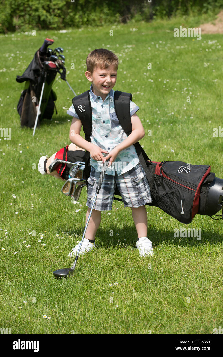 5 year old boy playing golf carrying his heavy bag of clubs, Hampshire