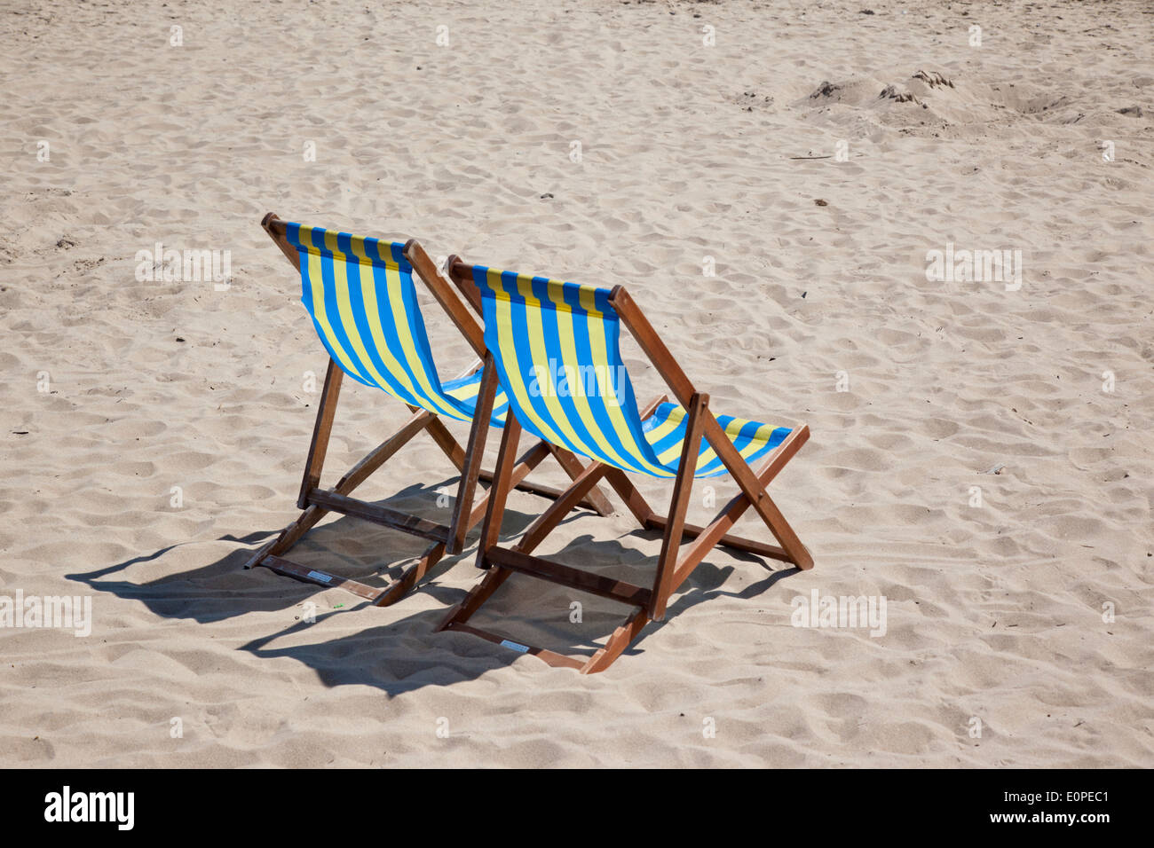 Pair of empty blue and yellow seaside deck chairs on the beach at Swanage, Dorset, England, UK Stock Photo