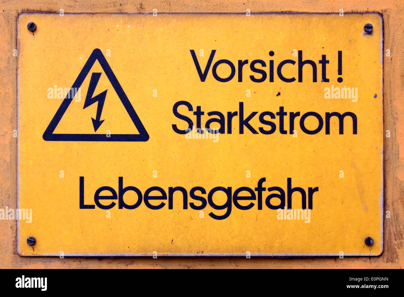 Weathered yellow German-language sign warns of high voltage (Starkstrom) at an industrial facility. Stock Photo