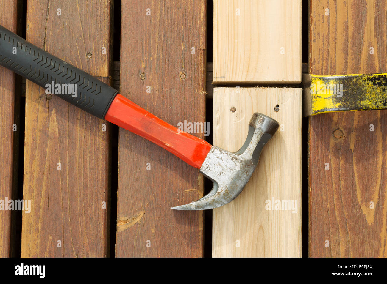 Horizontal photo of used hammer and pry bar aligning new boards for installing on cedar deck Stock Photo