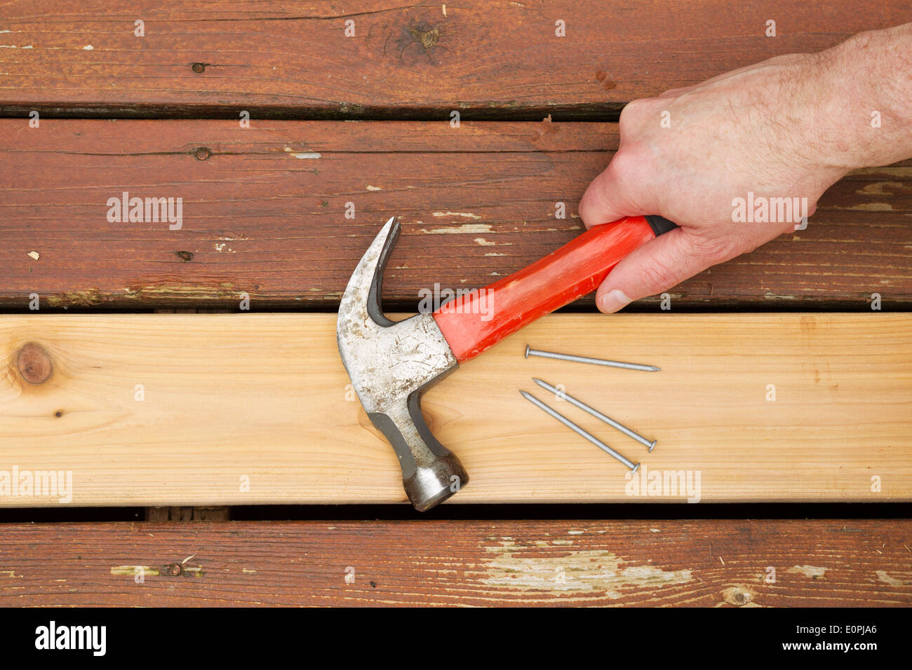 Horizontal photo of male hand picking up old hammer to install new cedar wood board into aging deck Stock Photo