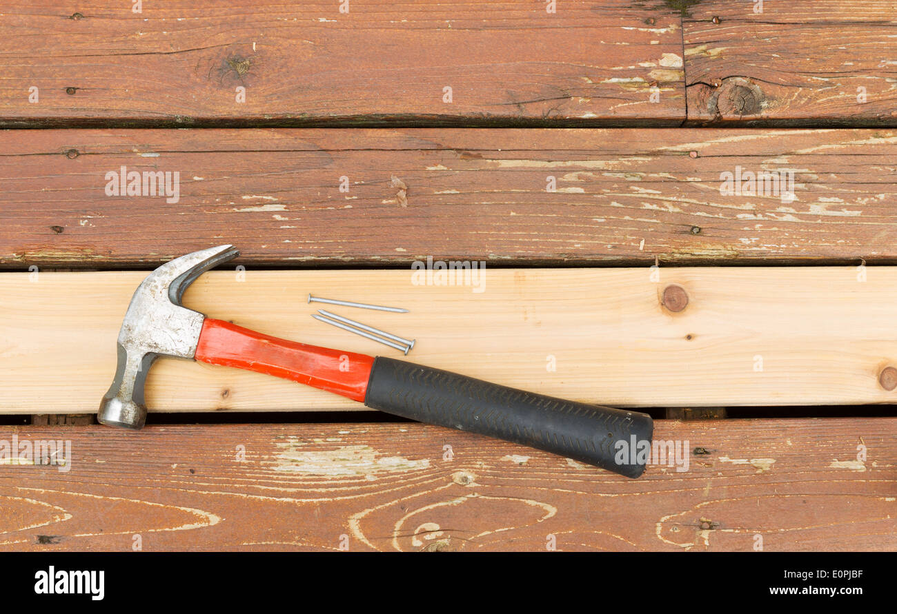 Horizontal photo of a single new cedar wooden board, with hammer and nails, next to fading wood on outdoor deck Stock Photo