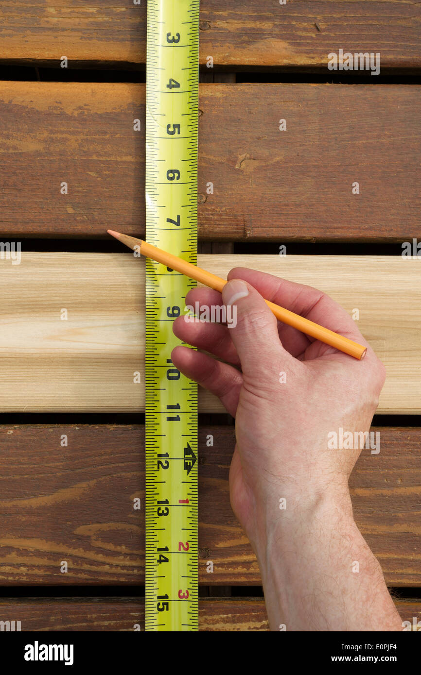 Vertical photo of hand with pencil and tape measuring space between new cedar wood boards on outdoor wooden deck Stock Photo