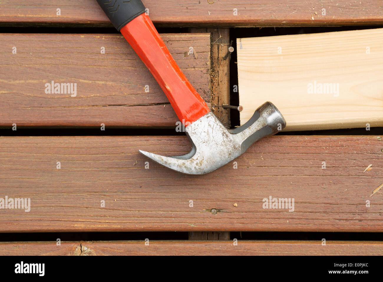 Horizontal photo of old hammer next to aged wood and exposed rusty nails with new cedar board being installed Stock Photo