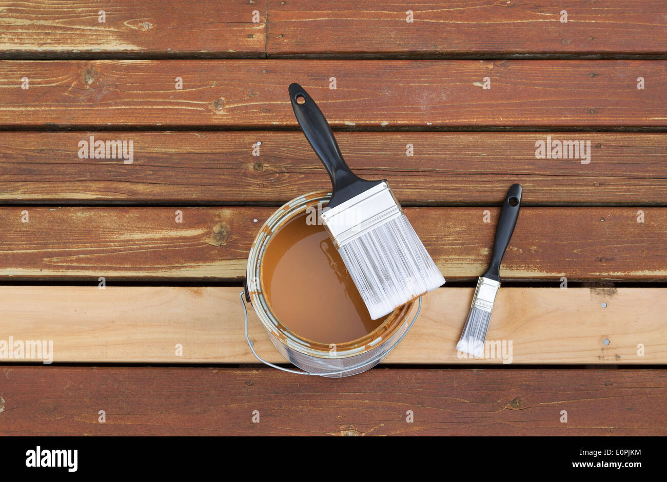Horizontal photo of large nylon paint brush on top of wood stain can with small paint brush lying on a single new cedar wood Stock Photo