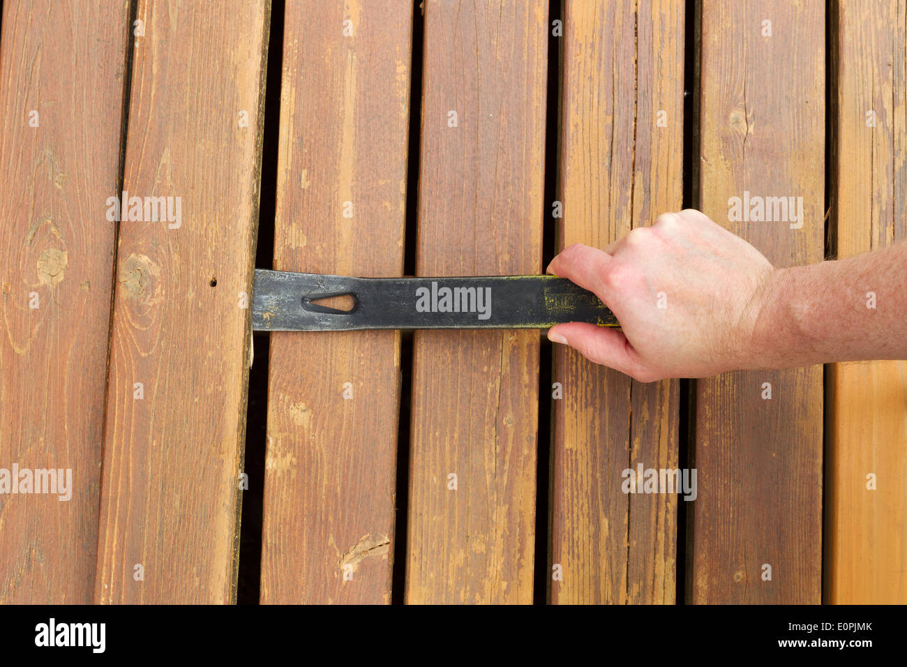 Horizontal photo of hand with pry bar lifting up old cedar wood board on outdoor wooden deck Stock Photo