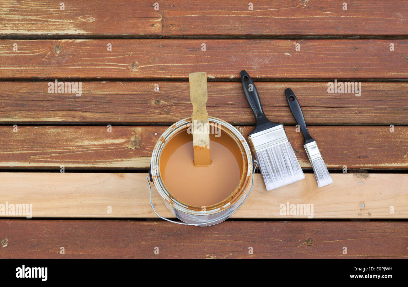 Horizontal photo of an open can of wood stain with two paint brushes lying on a single new cedar wooden board next to fading Stock Photo