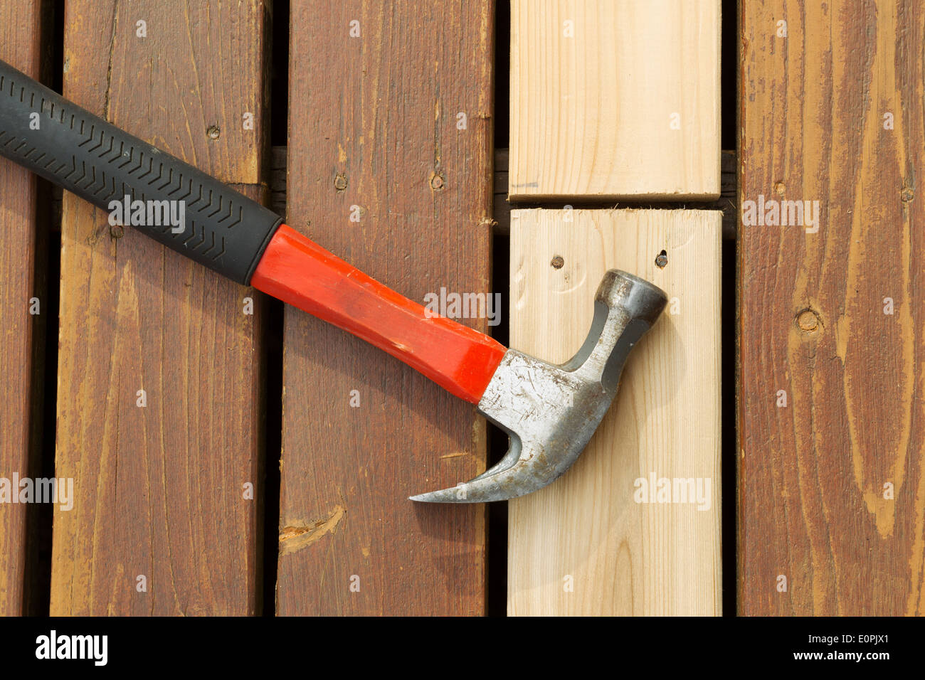 Horizontal photo of used hammer on top of newly installed cedar board next to aging deck boards Stock Photo