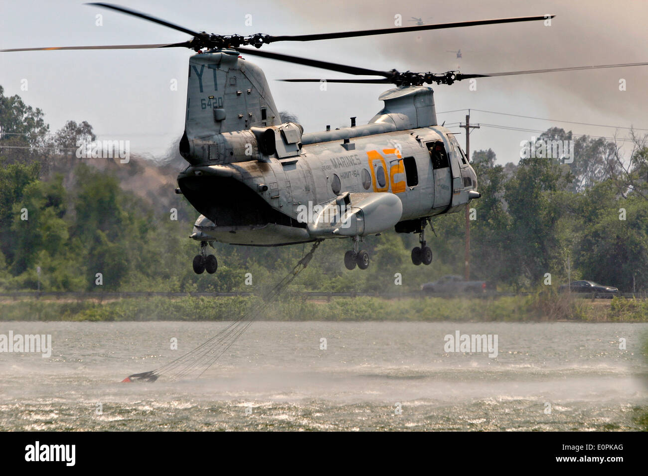 A US Marine Corps helicopter loads water into a Bambi bucket to help fight the Tomahawk and Las Pulgas wildfires as they burn the foothills May 16, 2014 around Camp Pendleton, California.  Evacuations forced more than 13,000 people from their homes as the fire burned across San Diego County. Stock Photo