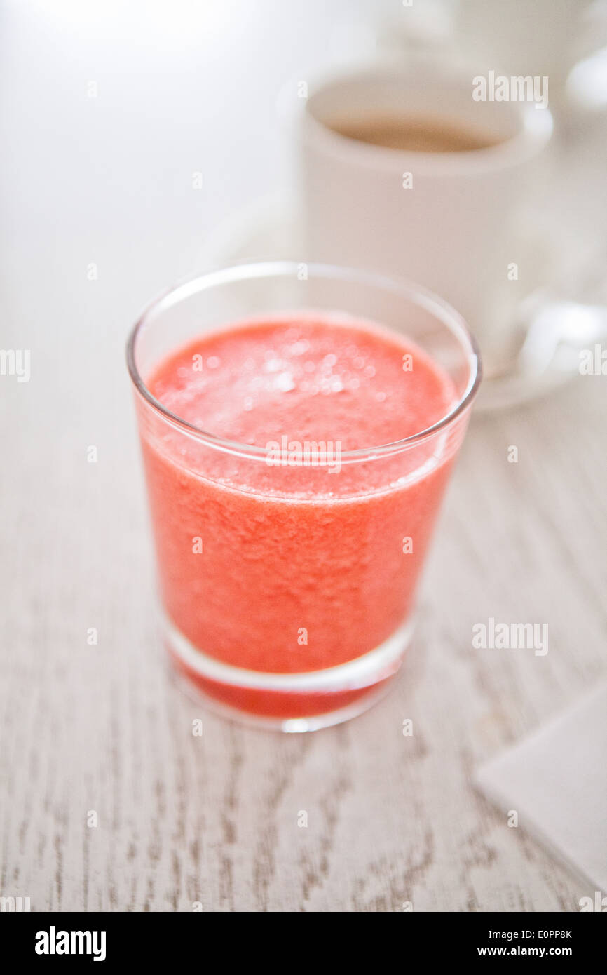 Closeup of strawberry smoothie in glass with cup of coffee in background Stock Photo
