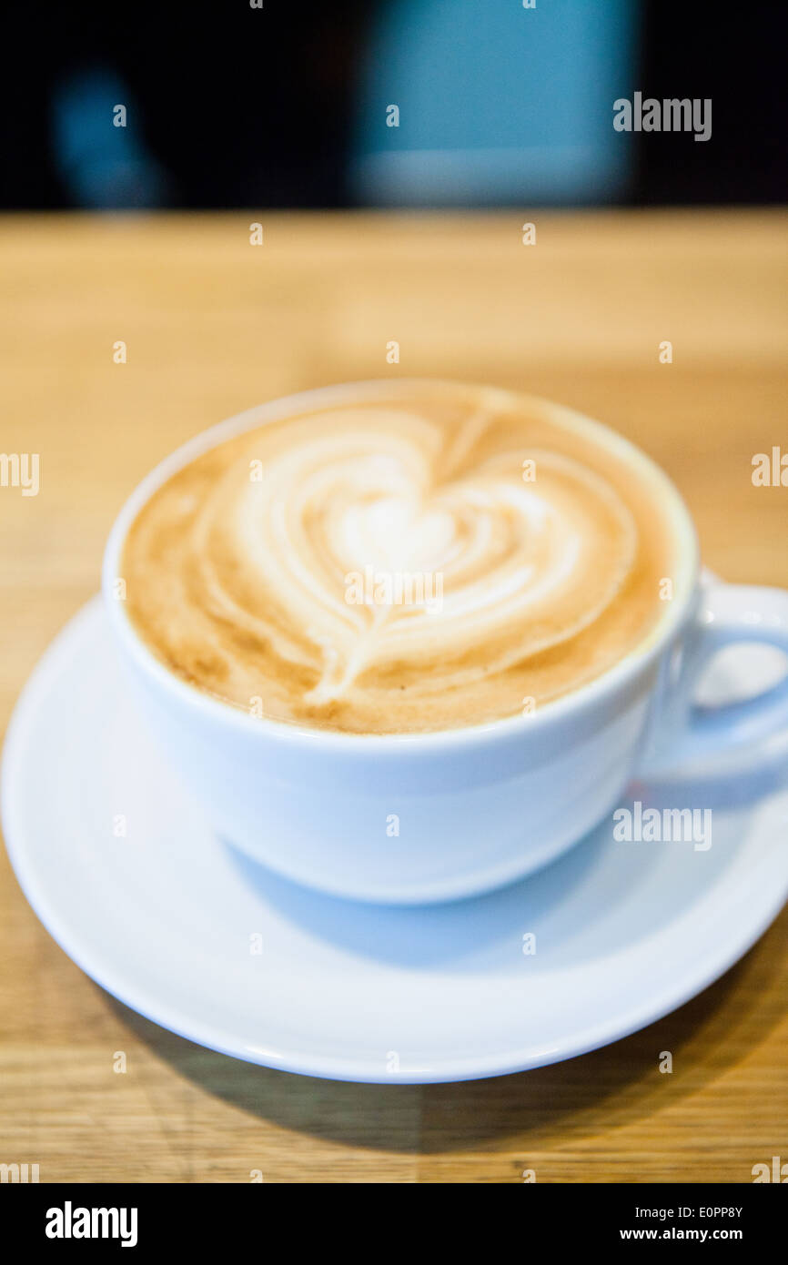 Closeup of espresso and milk based latte in cup with heart shape coffee art design on wooden table Stock Photo