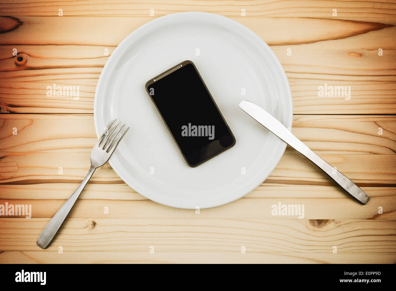 Mobile smart phone served as dinner on white plate. Concept of information absorption process. Stock Photo