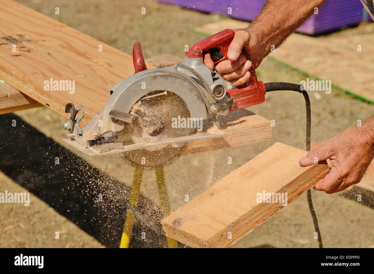 Building contractor worker using hand held worm drive circular saw to cut boards on a new home construction project Stock Photo
