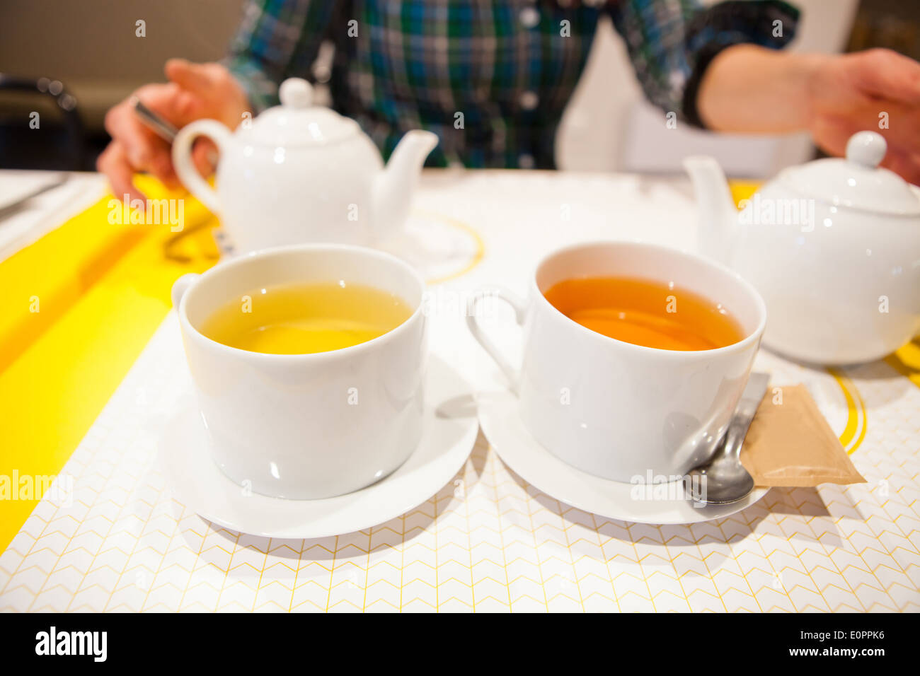 Closeup of two cups of herbal tea with tea pots and woman sitting in background Stock Photo