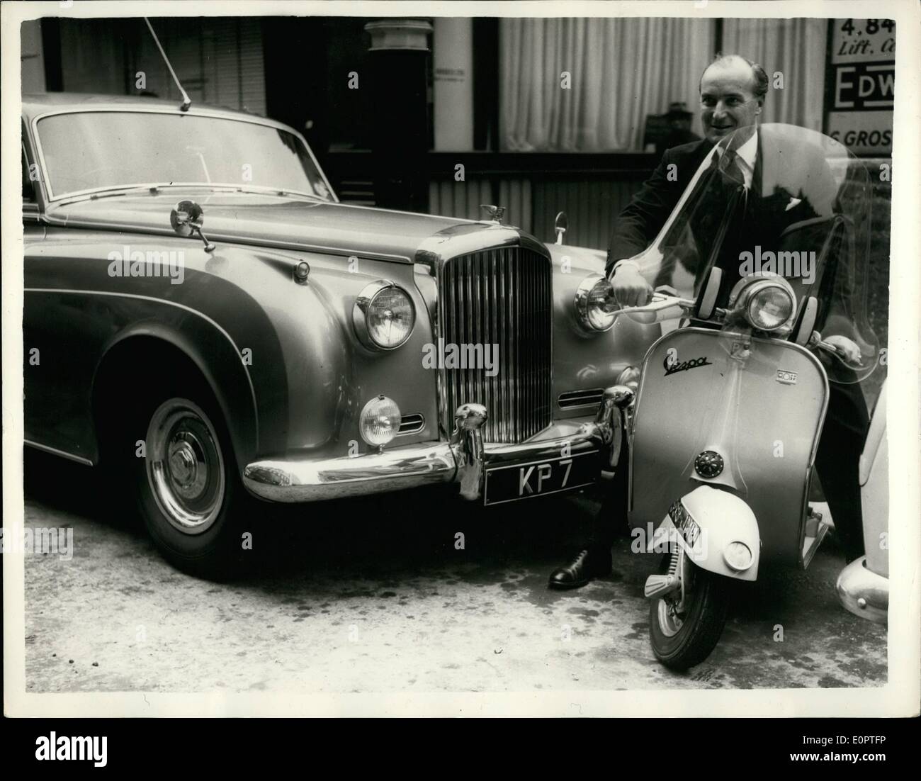 Dec. 12, 1956 - Preparing For The Worst: Mr. Peter Cadbury, Managing Director of Keith Prowse Ltd, of Bond Street, travels to his office in his Bentley car, and then uses his Vespa motor scooter for his business calls -- thus saving petrol. Photo Shows Mr. Peter Cadbury about to set off on his Vespa motor scooter, showing his Bentley car parked on left. Stock Photo