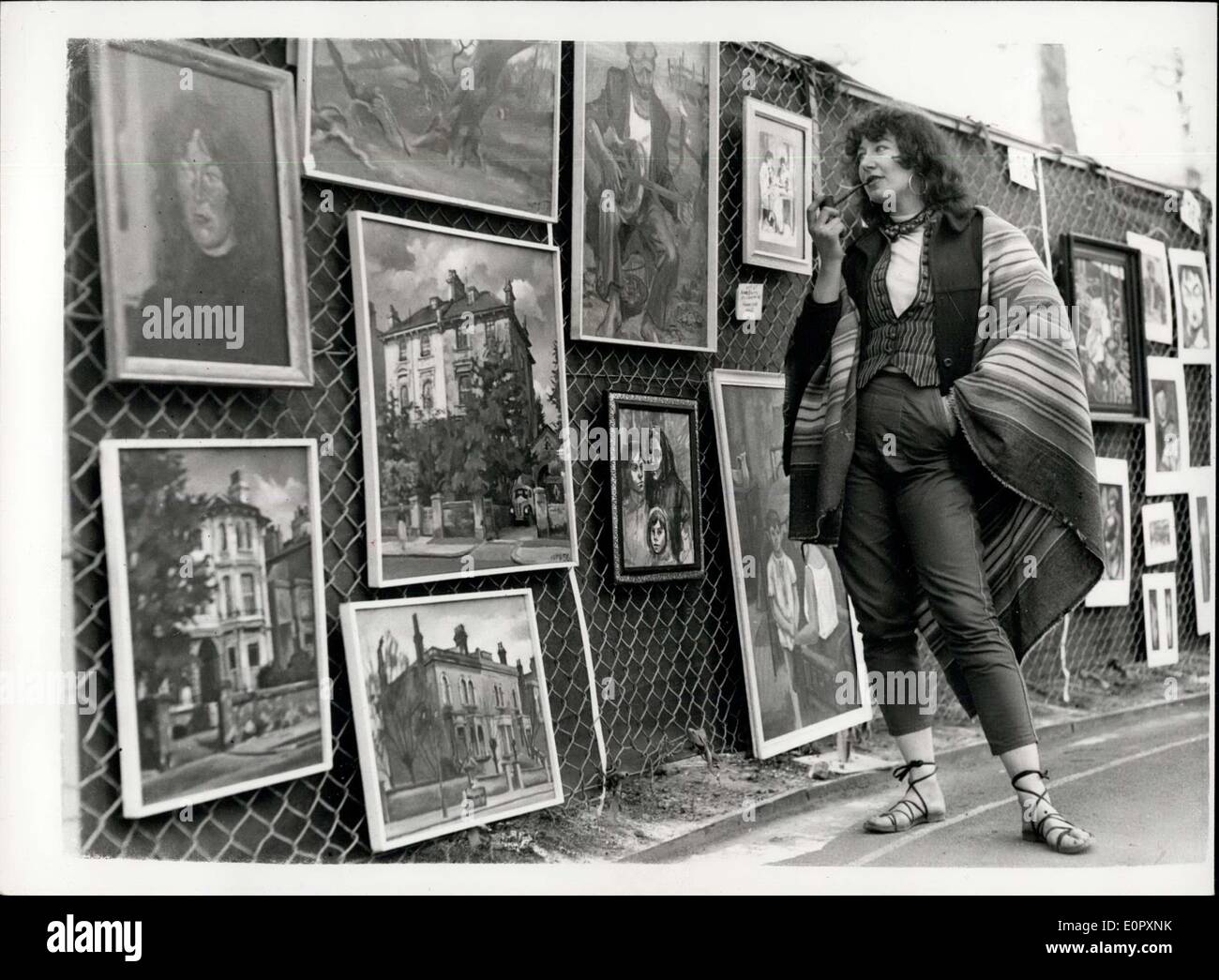 Apr. 27, 1957 - Open air art show in Embankment Gardens. The tenth annual display of paintings at the Victoria Embankment Gardens opened today. It is organized by the L.C.O. Photo shows Mrs. Anne Bulitis, of Homestead, smokes a pipe as she looks at her and her husband' exhibits- today. Stock Photo