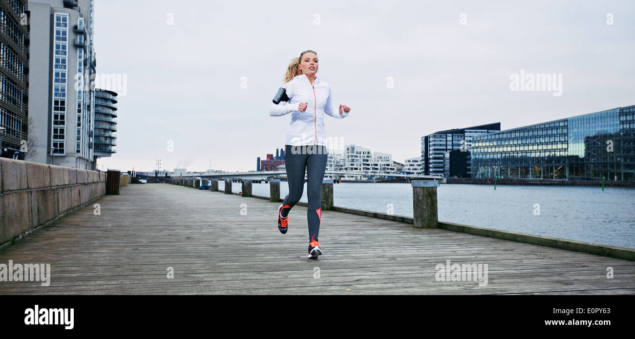 Young female athlete running on boardwalk along the river. Fit young woman jogging along the waterfront. Stock Photo