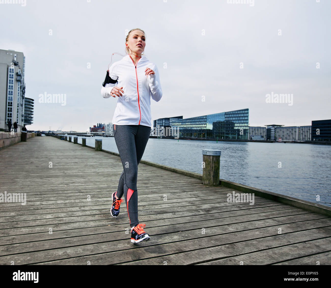 Female runner training outside. Caucasian female athlete jogging on boardwalk along river in city. Fit young woman running. Stock Photo