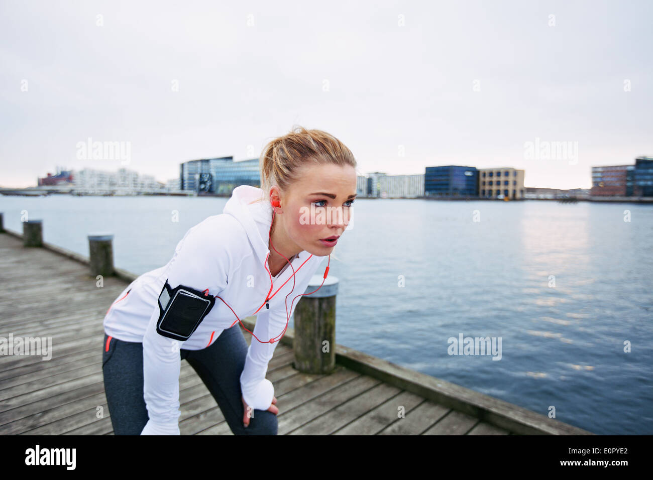 Female runner standing bent over and catching her breath after a running session along river. Young woman taking break after run Stock Photo