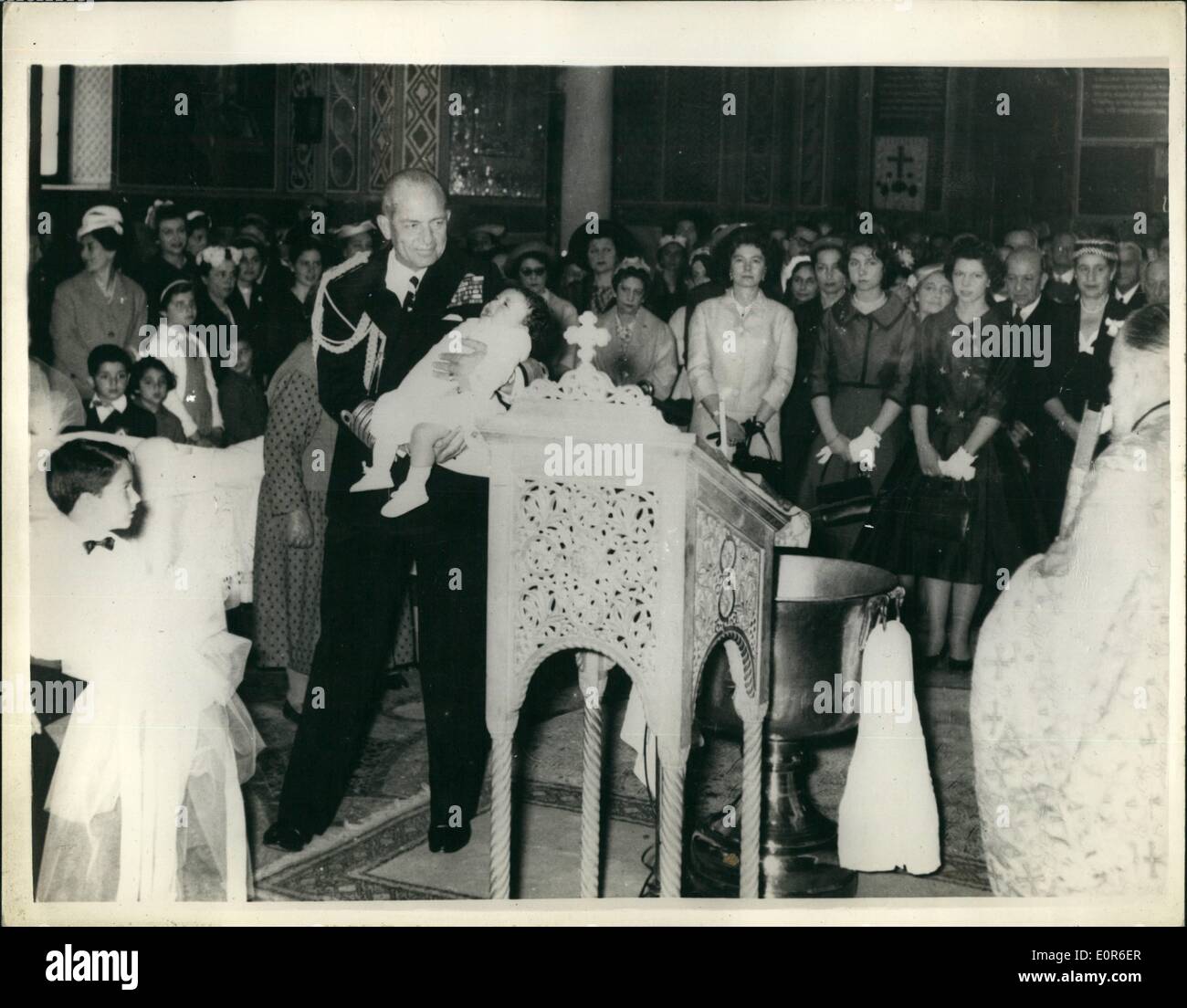 Jun. 06, 1958 - King Paul and Queen Frederica of Greece attended the baptism of the son of Captain and Mrs. Hors at the St Dionysius Church in Athens recently. Capt. Hors is former Adjutant of King Paul's. The child was given the names Paul George. Also present at the ceremony were the two daughters of the Royal couple, Princess Sophia, 20, and Princess Irene, 16. Photo shows King Paul holds his godson during the ceremony. In the back ground can be seen (L to R) : Queen Frederica, Princess Sophia and Princess Irene. Stock Photo