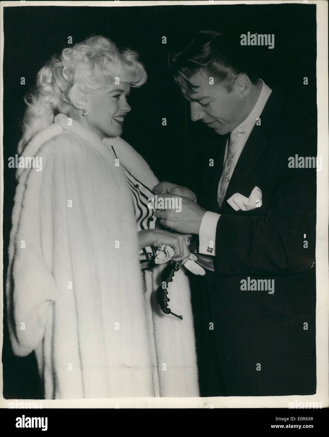 May 05, 1958 - JAYNE MANSFIELD AND HUSBAND FLY TO CANNES FILM FESTIVAL: Popular screen star Jayne Mansfield and her husband Micky Hargitay - left London Airport this morning - for the Cannes Film Festival. Photo shows Micky Hargitay comes to the assistance of his wife - when a button of her blouse broke - at the airport this morning. Stock Photo