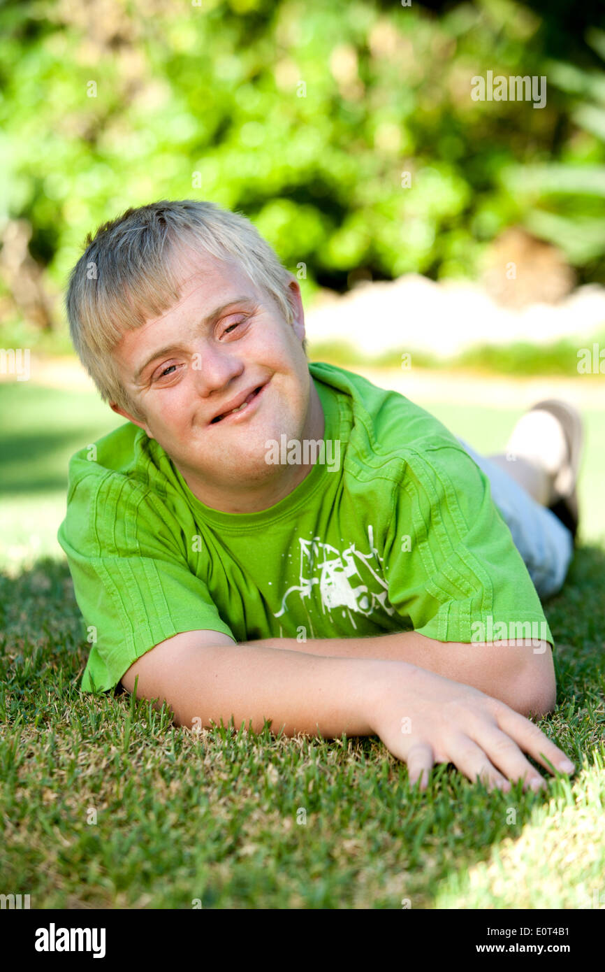 Portrait of cute handicapped boy laying on green grass. Stock Photo