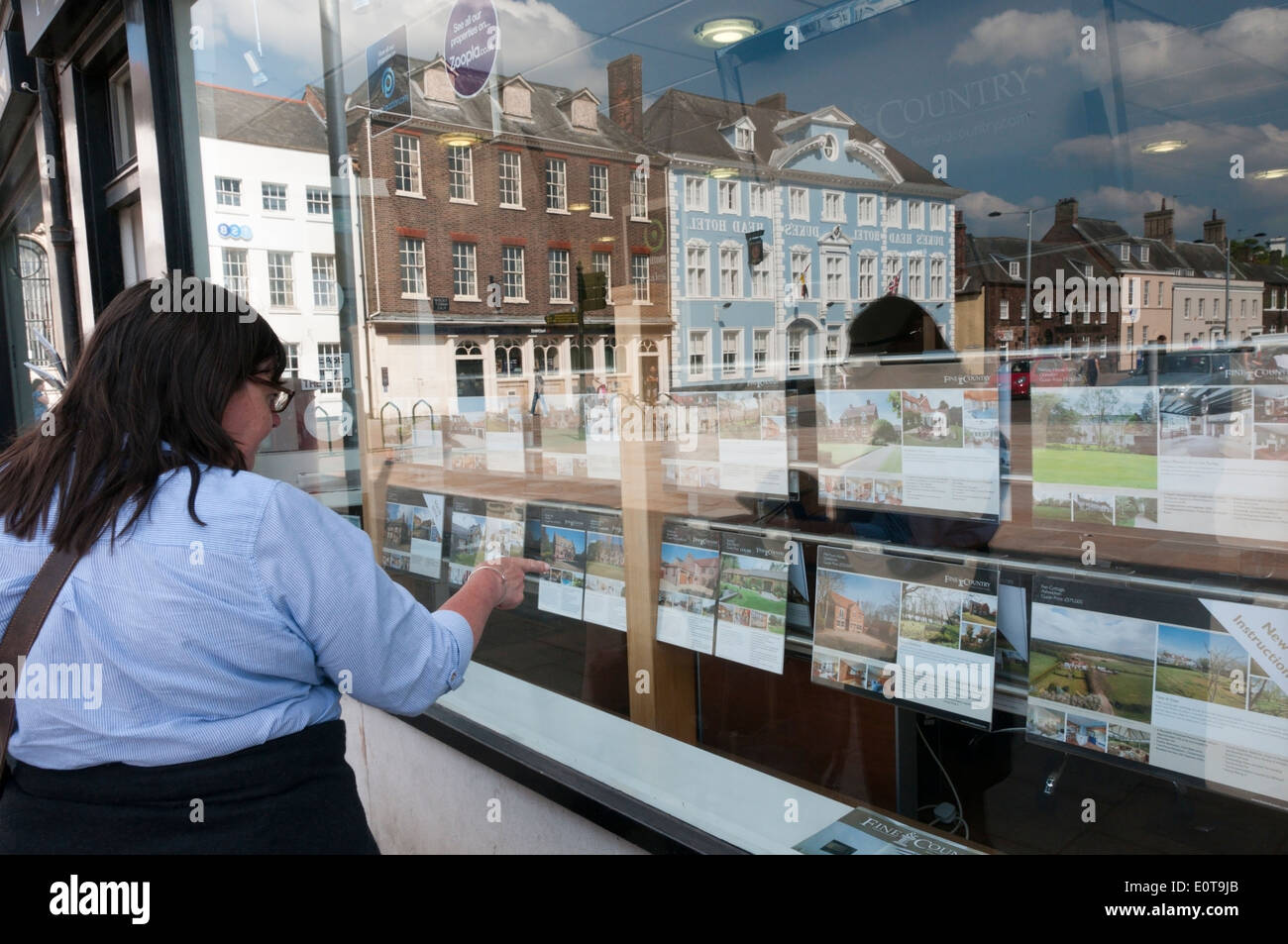 Woman looking in estate agent's window in King's Lynn with reflection of Tuesday Market Place. Stock Photo