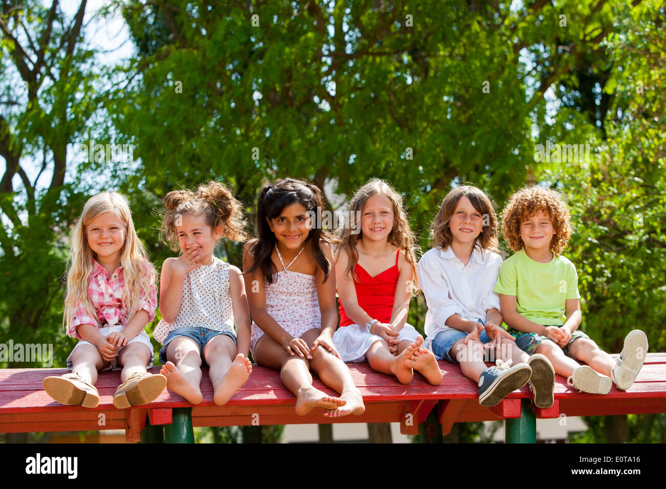 Portrait of happy children sitting together wooden structure in park. Stock Photo
