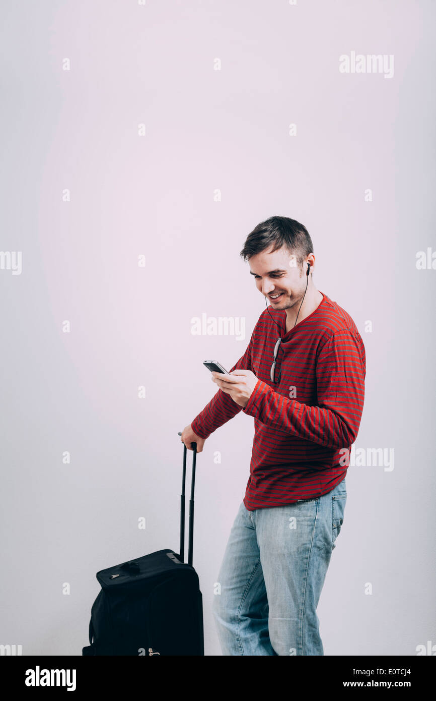 Happy casual man traveling with luggage and using mobile phone. Stock Photo