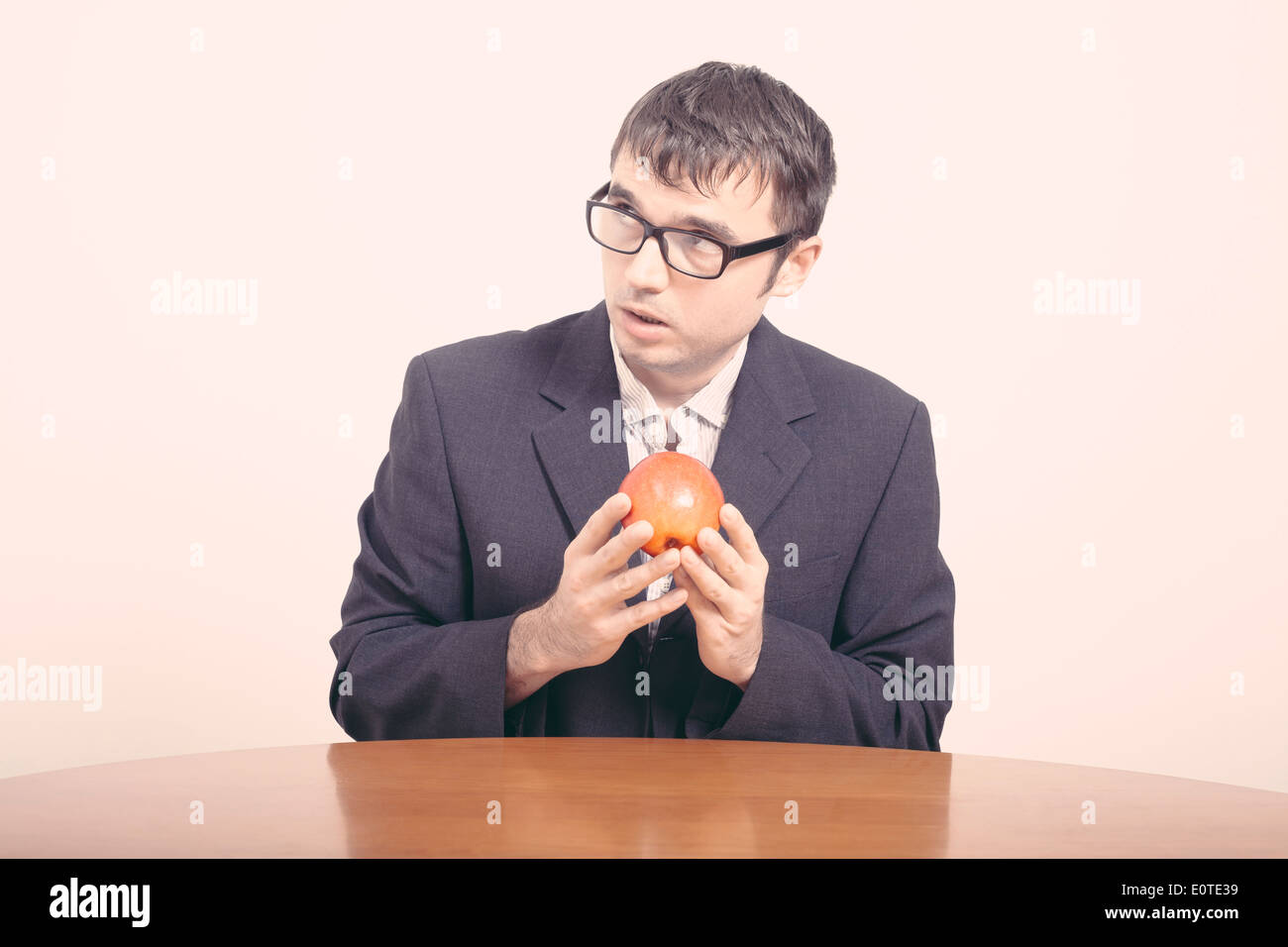 Worried businessman sitting behind table and holding apple. Stock Photo