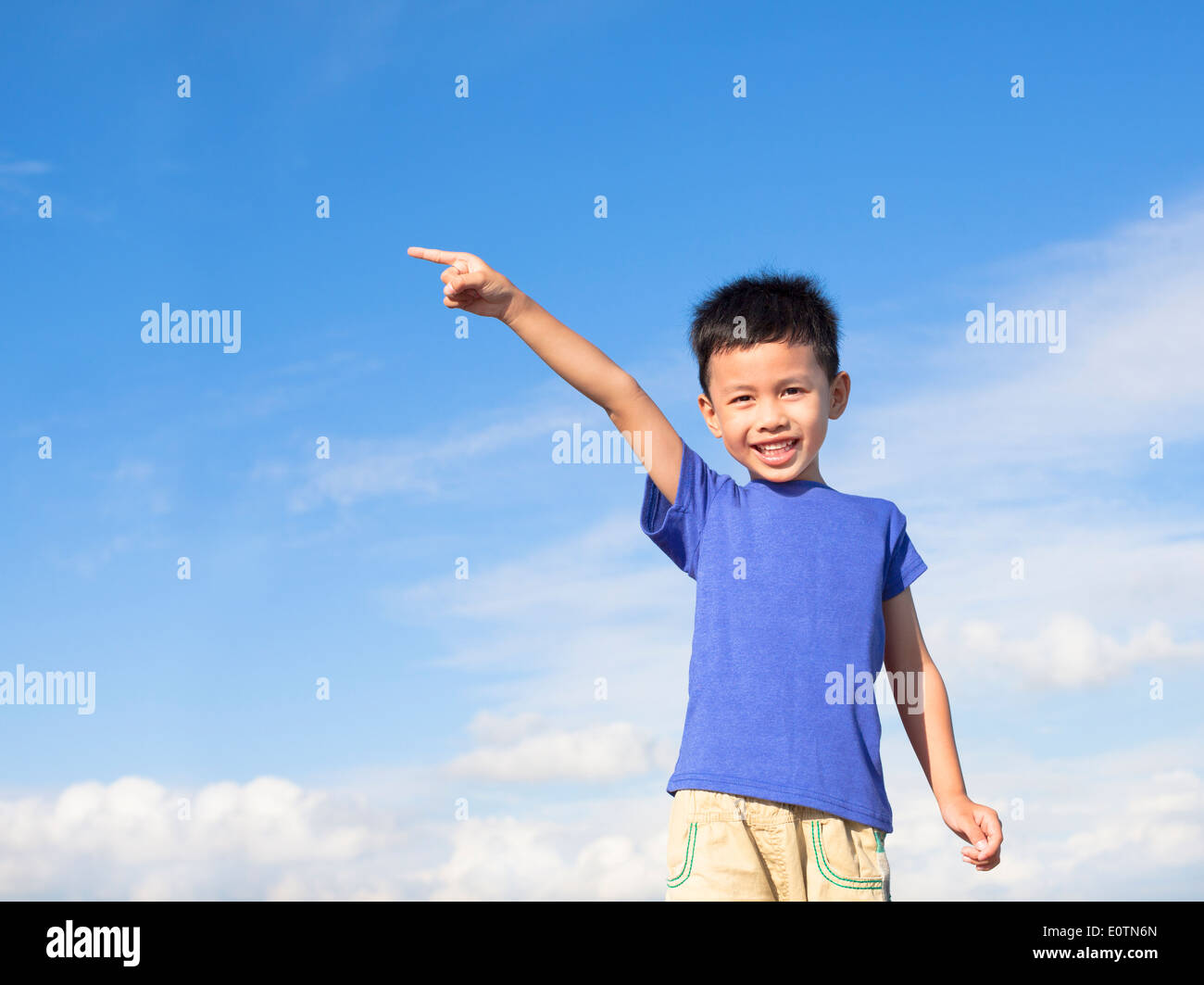 happy little boy pointing direction with blue sky background Stock Photo