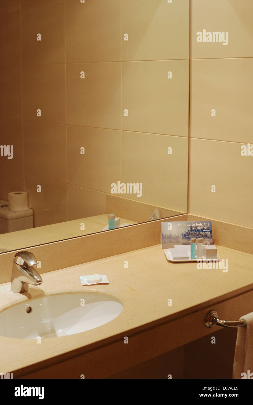 Modern hotel bathroom showing sink and mirror with environmental message about towel washing Stock Photo