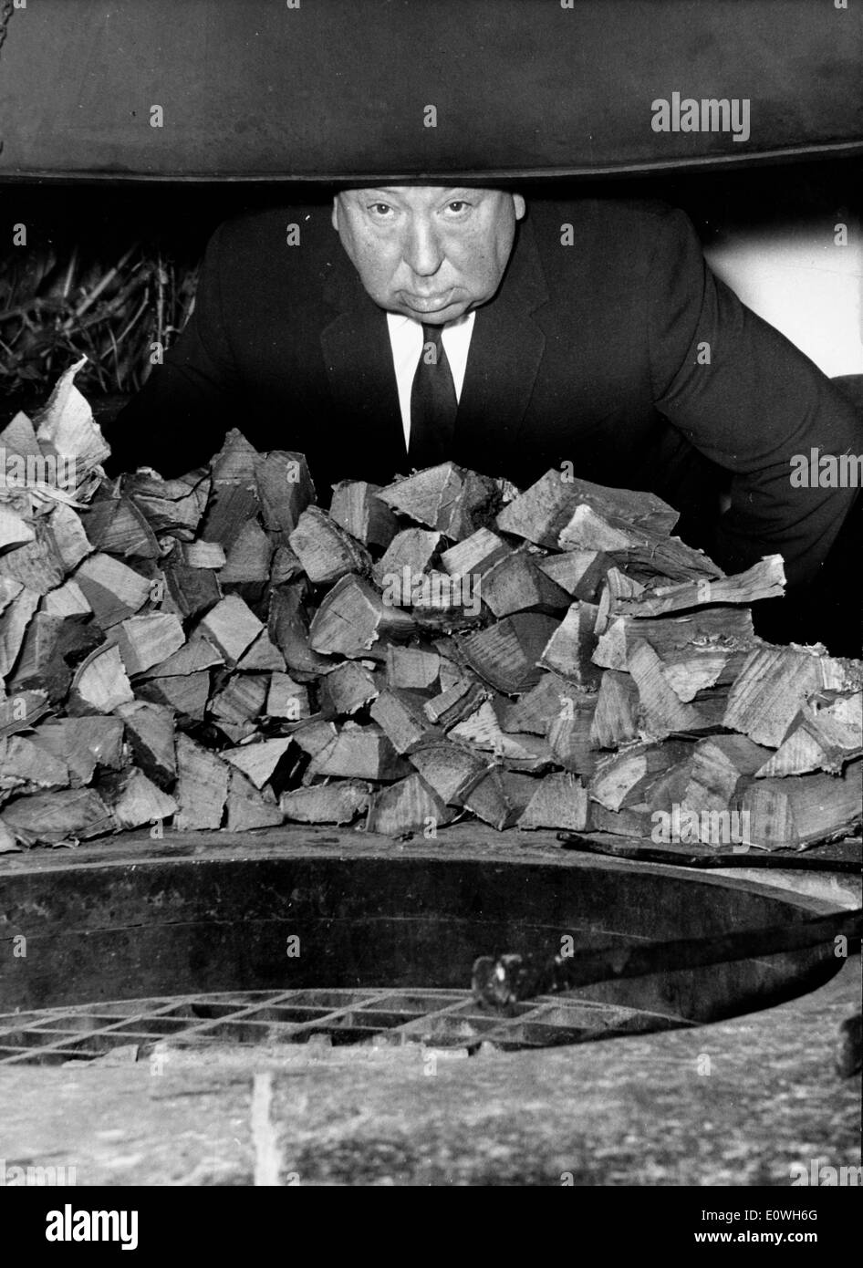 Film maker Alfred Hitchcock ducking behind a pile of wood Stock Photo
