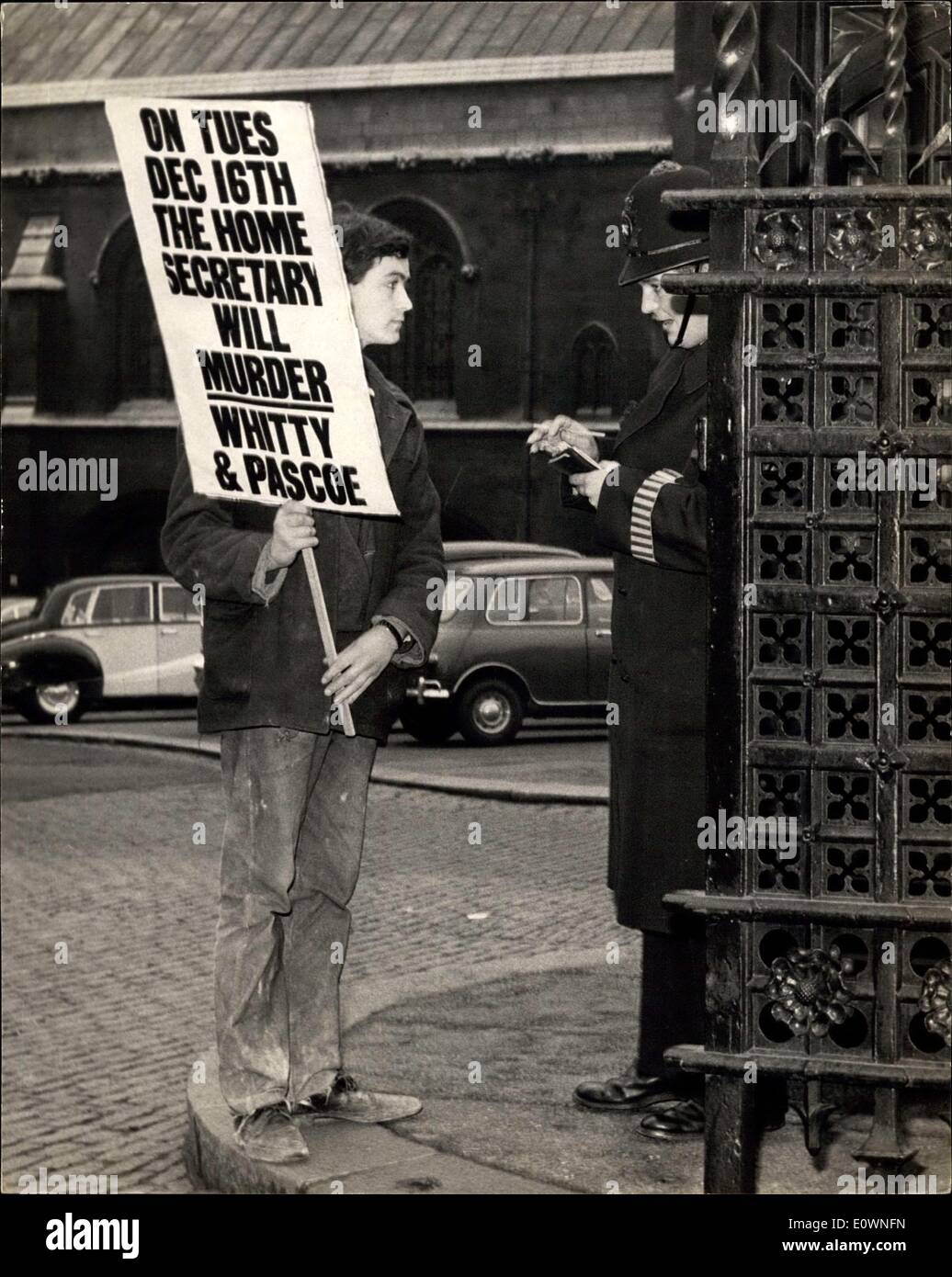 Dec. 16, 1963 - Demonstrator has his name taken - outside house of Commons....Protesting Against Tomorrow's Executions: Police took the name this afternoon of Timothy Fox - who was to be seen parading outside the House of Commons - protesting against the hanging tomorrow morning of murders - Dennis John Whitty (22) and Russell Pascoe (23). They killed 64 year old farmer William Rowe at his lonely farmhouse on the Lizard Peninsula - and ransacked his home. Photo Shows Police talk with Timothy Fox - at the gates of the house of Commons this afternoon. Stock Photo