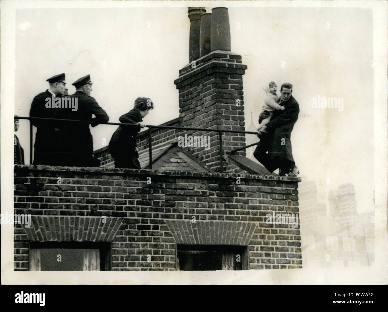 Mar. 03, 1964 - MAN WITH A CHILD IN HIS ARMS THREATENS TO JUMP FROM THE ROOF OF A THREE STOREY BUILDING. Fireman and police were called to Marchmont Street, Bloomsbury, this evening, when a man with a baby in his arms threatened to jump from the roof of a three storey building, talking the child with him. A crowd of several hundred people gathered below as Woman police Constable Margaret Clelland, who had been trying to reason with the man, drew closer to him and grabbed the baby from his arms. Four other policemen rushed forward and grabbed the man Stock Photo