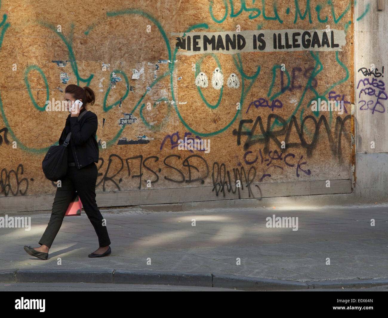 Woman talking on mobile phone with graffiti saying nobody is illegal in Dutch language, Brussels, Belgium Stock Photo