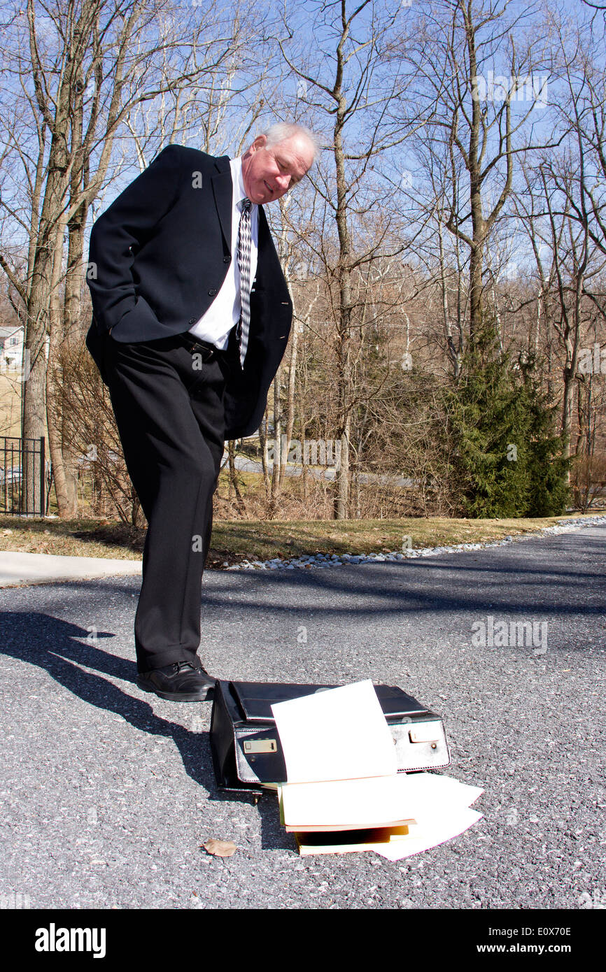 Businessman kicking his fallen briefcase on the ground on an empty road as in disgust or quitting Stock Photo