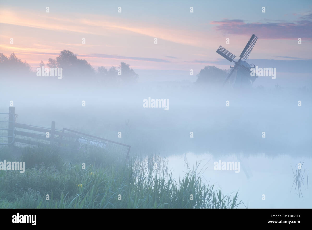 misty sunrise over Dutch windmill on farmland, Netherlands Stock Photo