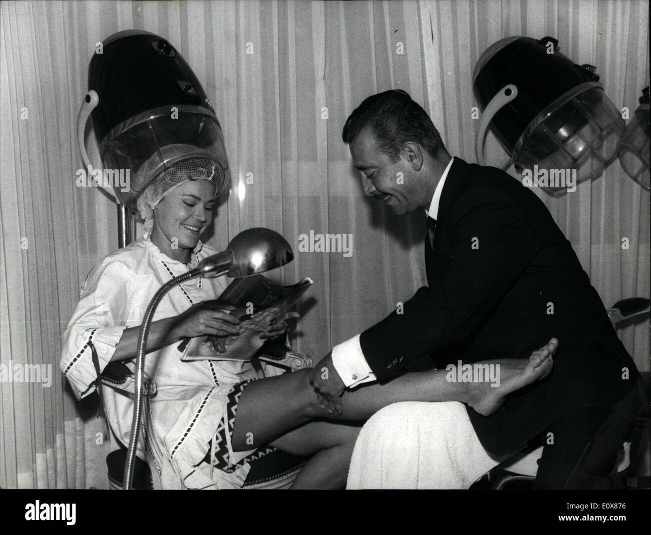Sep. 09, 1965 - Paris Hair stylist has bright ideas: Claude Maxime is not only a top hair stylist but he also has ideas of him own. To keep abreast with the new Fashion of Short skirts launched by courreges he offers his fair clients a knee massage while they are waiting for their hair to be tried under the helmet. Photo shows Claude Maxime massaging the knees of a client. Stock Photo