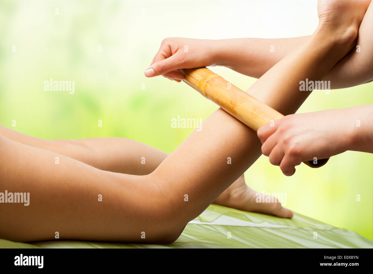 Therapist massaging female legs with bamboo stick. Stock Photo
