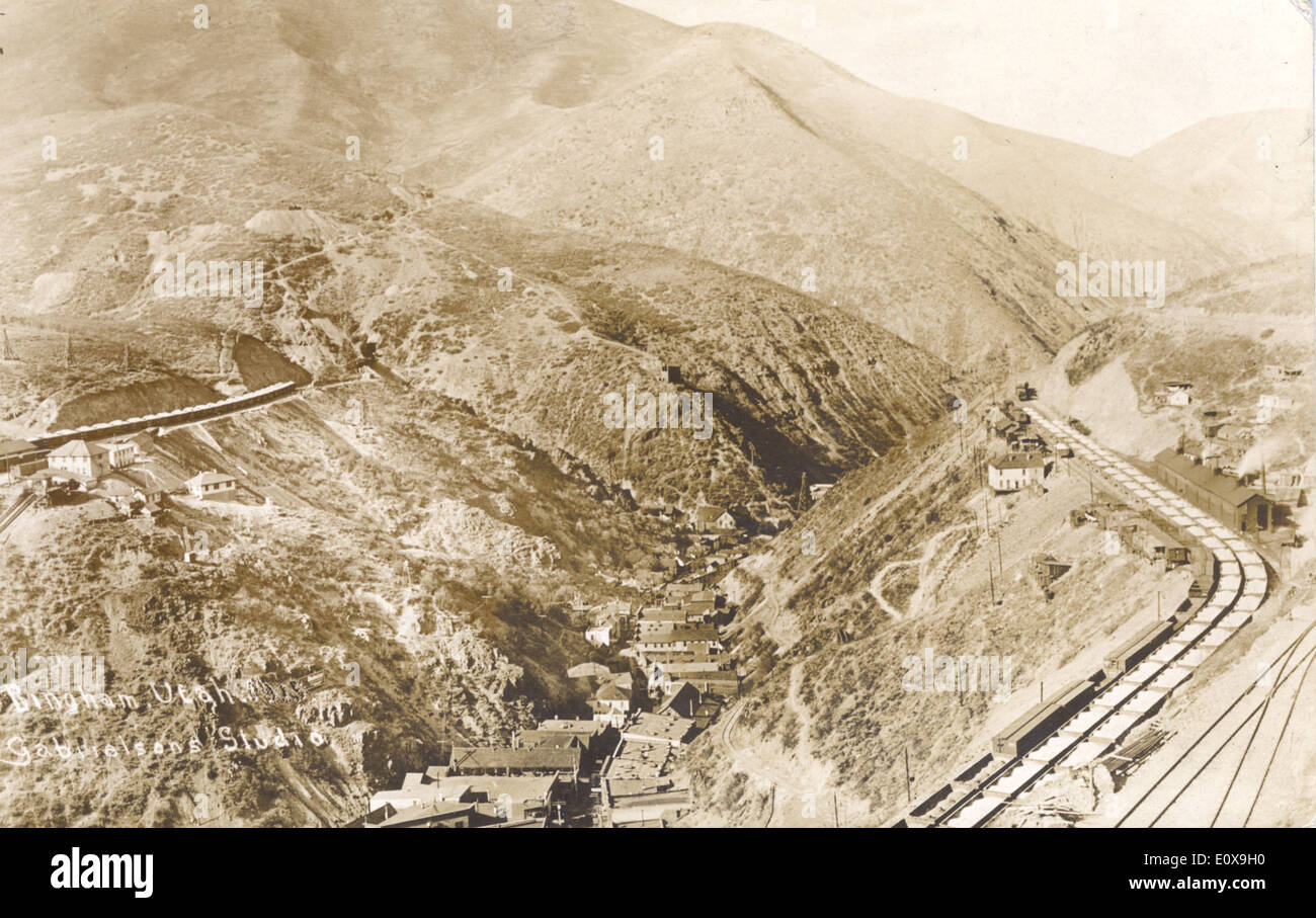 Aerial view of Bingham Canyon, Utah, showcasing the sprawling landscape, mining operations, and the surrounding towns. The view highlights the Bingham Canyon Mine, one of the largest open-pit copper mines in the world. Visible also are various railroad tracks used for transporting materials, with the town of Bingham and other nearby areas spread across the region. This historical photograph captures a significant part of Utah's industrial landscape. Stock Photo