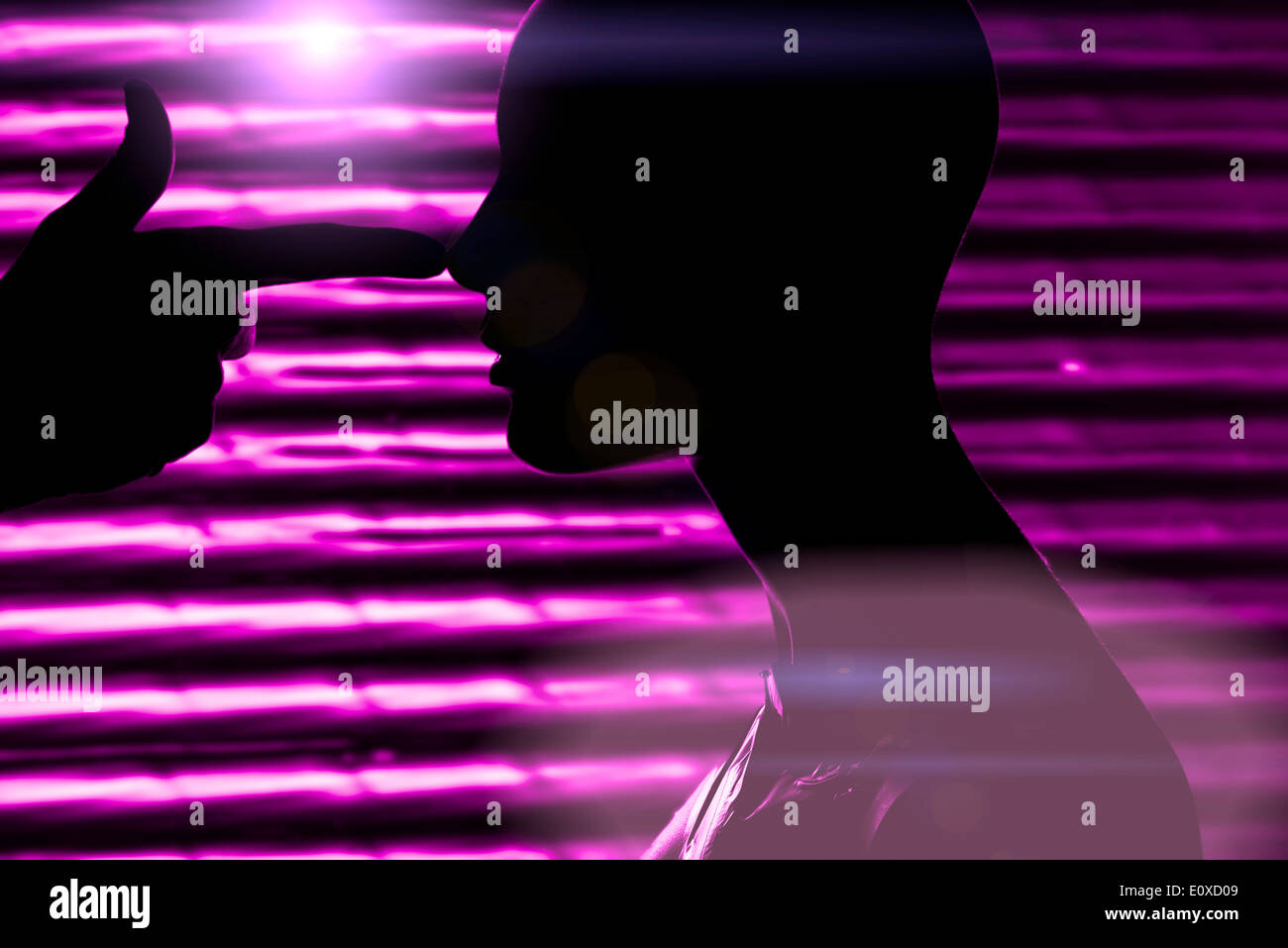 Silhouette of head of mannequin and hand of a man making a threatening gesture imitating a gun pointed at the female dummys head. Night club setting with purple light. Stock Photo