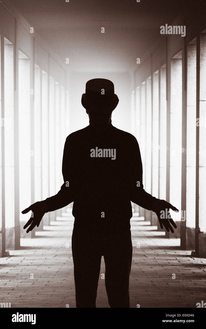 Silhouette of man with hat standing in backlit colonnade showing his hands. Conceptual image of magic, mystery and the paranormal. Stock Photo